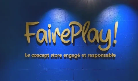 Enseigne lumineuse de magasin "FairePlay!" avec slogan "Le concept store engagé et responsable" sur mur bleu éclairé par spots